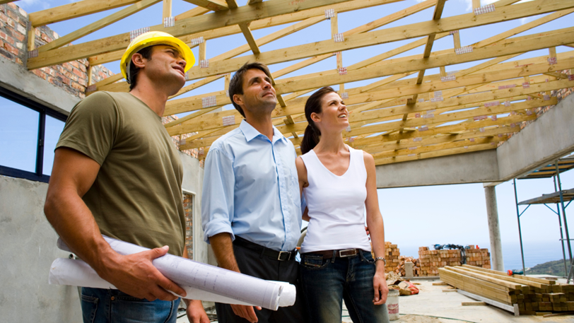 Two clients and a general contractor stand in the framework of a new home.