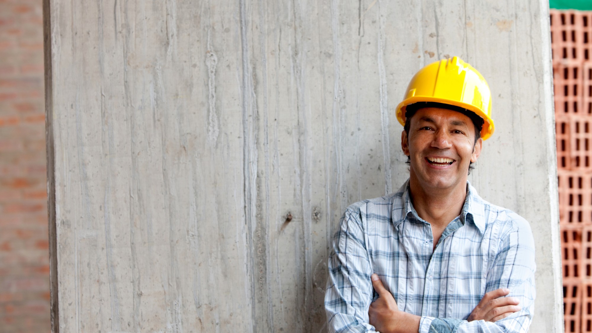 A contractor in yellow hard hat and blue plaid shirt smiles.